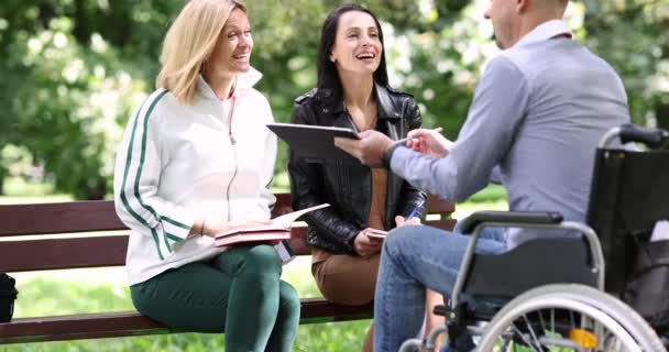 휠체어에 장애를 남자는 태블릿의 화면을 보여줍니다 날씨에 공원에서 친구와 사이의 — 비디오