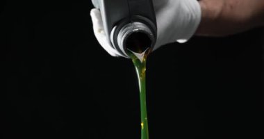 Beyaz eldiven giyen tamirci siyah arka planda plastik şişeden motor yağı döküyor. Araç motoru için yağlayıcı garajda yavaş çekimde