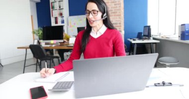 Kulaklıklı ve mikrofonlu bir kadın dizüstü bilgisayar 4K filminde çalışıyor. Çağrı merkezi konseptinde çalış