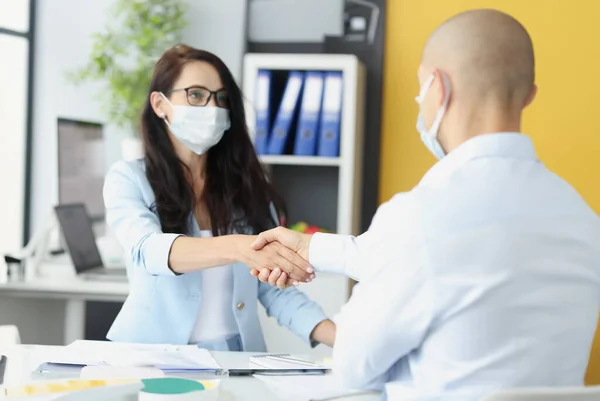 Young business people in medical masks shake hands at work table. Safe distance and communication for health concept