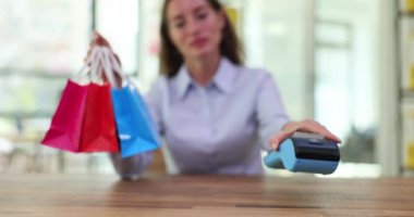 Mağazadaki kadın POS terminalini müşterilere teslim ediyor. POS terminalinin kurulumu ve kullanım şartları. Cep telefonu aygıtınızı kullanarak satın alma ücretini ödeyin