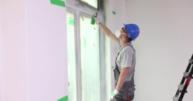 Boyacı cam katmanını beyaz sprey boyayla boyuyor. PVC pencere ve pencere eğimlerinin boyanması