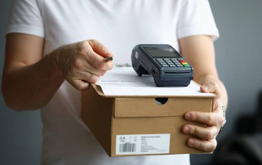 Kurye ödeme terminali ve kalemle dokümanlarla dolu karton bir kutu tutuyor. Paket teslimatı ve elektronik ödeme kavramı