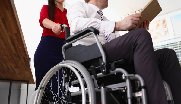 Woman rolls man in a wheelchair in office. Businessmen with disabilities concept