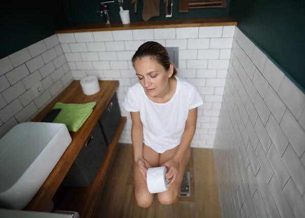 여자는 변기에 앉아서 화장지를 — 스톡 사진