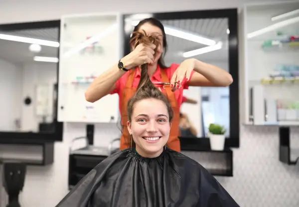 Portrait of smiling woman in hairdressing salon, which master cuts her hair. Womens haircuts and styling in a beauty salon concept
