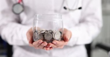 Beyaz önlüklü doktor bozuk para kavanozunu tutuyor. Sağlık sigortası kavramı