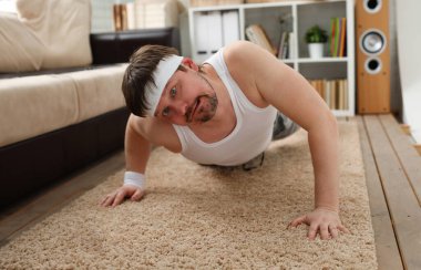 Aşırı kilolu genç yakışıklı bir adam evdeki ilk spor salonunu halıda yapıyor. Söndürüldü ve aşırı yüklendi. Kilo vermeye teşvik etmiyor..