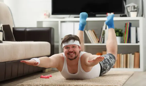 Young attractive fitness man lies on a fat mat with overweight performs exercises and smiles