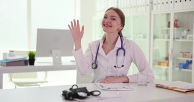 Kameraya bakıp kameraya el sallayan gülümseyen doktorun portresi. Tıbbi terapist hastalarla sanal online görüşmede uzaktan danışmanlık yapıyor.