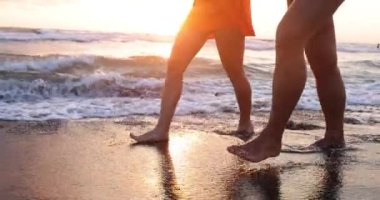 Erkek ve dişi ayakları gün batımında ya da şafakta denizde yürüyor. Balayı ve romantik kaçamak