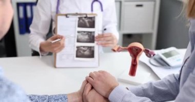 Evli çift ultrasonda hamile kadını muayene ediyor. Doktor bebeğin ultrason görüntüsünü inceliyor ve gelecekteki ebeveynlerin sorularını cevaplıyor.