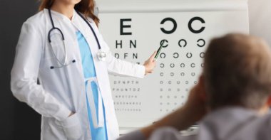 Profesyonel göz doktoruna yakın çekim. Hastanın görüşünü kontrol ediyor. Görme testi masasındaki harfi işaret eden deneyimli göz doktoru. Sağlık ve önleme kavramı