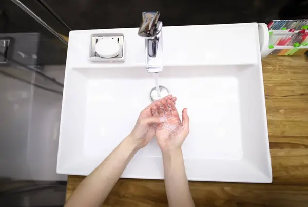 水の下で石鹸で手を洗う人のトップビュー 感染の予防が広がる 白のモダンな蛇口をきれいにします シルバークレーン 浴室と個人衛生の概念 — ストック写真