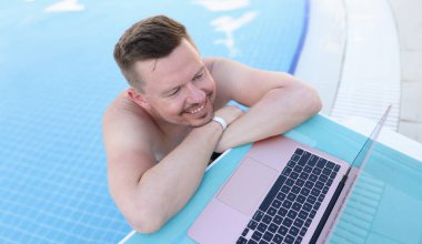 Young handsome man in pool with laptop. Remote work freelancer works anywhere in world