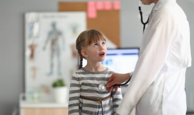 Smiling girl at doctor office in clinic. Female pediatrician examining small child with a stethoscope