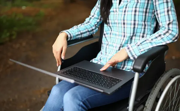 Woman in wheelchair in park with laptop on lap closeup. Remote work freelance and training for the disabled