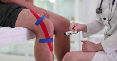Pratisyen, muayene odasında refleks çekiç diziyle ve kineziyoloji esneme bandıyla vuruyor. Şişkinliği ve acısı azalmış bir adam. Travma doktoru hastanede.