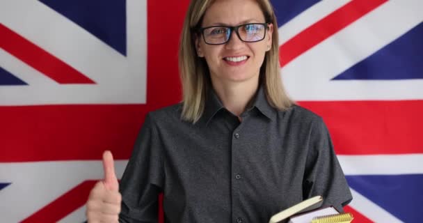 ブロンドの女性は 言語学習を促進します イギリスの国旗の前に立つ陽気な英語講師と 学生がゆっくりとした動きを学ぶことを奨励 — ストック動画