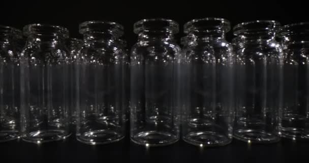 ワクチン接種のための空のガラス瓶は暗い部屋の黒い表面に並んでいました ブラックスタジオの医療用ガラス製品のコンセプト — ストック動画