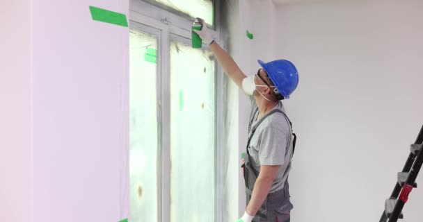 Ein Behelmter Bauunternehmer Sprüht Graue Farbe Auf Fensterrahmen Von Wohnungen — Stockvideo
