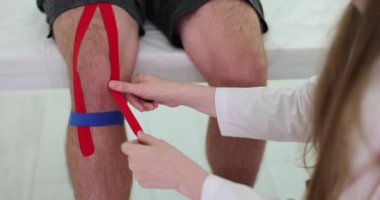 Fizyoterapist, erkek hasta dizine kinesio bandı uyguluyor. Kineziyoloji fizyoterapi ve rehabilitasyon