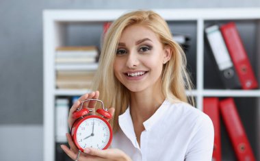 Çalar saat üzerinde elinde tutan bir kırmızı renk sabah 8 oclock gösterilen veya Pm önce akşam gülümseyen iş kadın