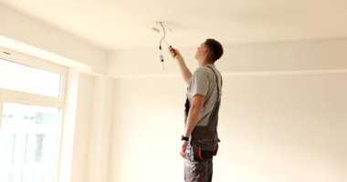 Adam odada silindirle tavanı beyaza boyuyor. Tavan duvarlarını boyama aşamaları ve sürecin ayrıntıları