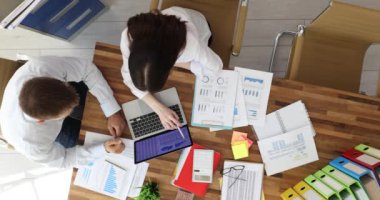 İş adamı ve iş kadını bir dizüstü bilgisayar ve belgelerle masada oturuyor ve iş yerinde birlikte çalışıyorlar. İş ekibi stratejileri, planları ve analitik ilerlemeyi tartışıyor