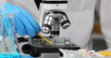 Bilim adamı kimyager mikroskop yakınındaki cam kaydırağında sıvının asitliğini kontrol etmek için litmus kağıdını kullanıyor. 4k film yavaş çekim. Kimyasal deneyler konsepti