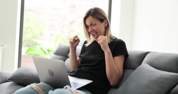 女人坐在家里的笔记本电脑前 从社交网络4K电影慢动作的好消息中欢欣鼓舞 祝好运和积极向上的情绪观念 — 图库视频影像