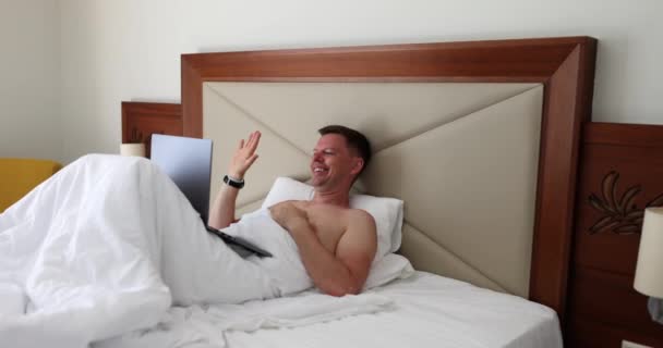 Чоловік Лежить Ліжку Ноутбуком Махає Рукою Екрані Фільм Повільний Рух — стокове відео