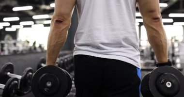 Spor salonunda dambıllar taşıyan erkek sporcu. Yakın çekim 4K yavaş çekim. Sağlıklı yaşam tarzı ve spor anlayışı
