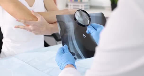 Arzt Traumatologe Hält Röntgenbild Des Ellenbogengelenks Und Lupe Vor Kranke — Stockvideo