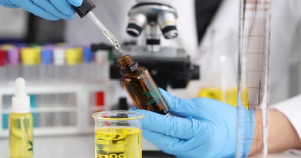科学者の化学者は実験室4K映画で瓶からガラス製のビーカーにマリファナ油を滴下 化粧品コンセプトの品質管理 — ストック動画