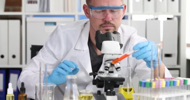 戴着防护眼镜的科学家化学家拿着装有血液的试管 通过显微镜检查4K膜 对照头孢病毒概念开发制药工业药物 — 图库视频影像
