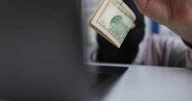 Siyah maskeli siber suçlu dolarları kancada tutuyor ve bilgisayara bakıyor. Ağ dolandırıcıları ve dolandırıcılık konsepti