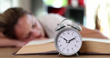 Açık kitaptaki kadının çalar saati yalan söyler ve masada uyur. Fazla çalışma, uykusuzluk ve aşırı çalışma