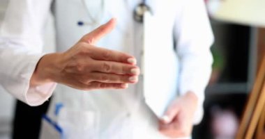 Doktora yardım eden kadın eli, el sıkışmak ve selamlaşmak için kameraya uzanıyor. Sizi toplantıya ve tıbbi danışmaya davet ediyor.