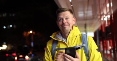 Akıllı telefonu tutan ve toplantı sırasında el sallayan genç ve mutlu bir adam. Turist blogcusu şehirde buluşuyor