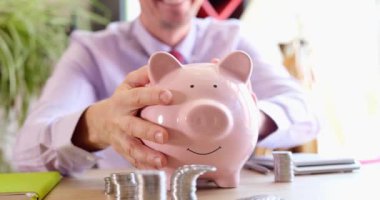 Finansal domuzlarla dolu kumbarayı okşayan neşeli iş adamı. Kârlı mali yatırımlar ve bütçe