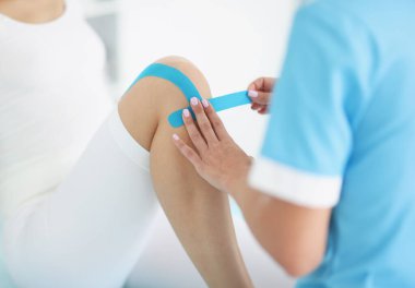 Doktor hastaların dizlerine kinesio bandı yapıştırıyor. Eklemlerde ve kaslarda yaralanma ve burkulma kavramı