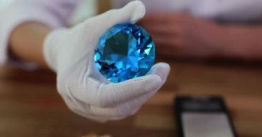 Mücevher aletlerini kullanarak elmasları derecelendirme sürecinde elmas uzmanı ellere yakın çekim. Büyük güzel mavi safir.