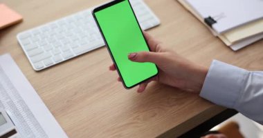 Ofisinde yeşil ekranlı akıllı telefonu olan bir kadın. Mobil uygulamalar ve cep telefonu kullanımı