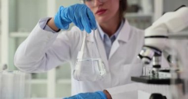 Bilim adamı şeffaf sıvıyla matarayı tutuyor ve elleriyle çeviriyor. Kimyasal, şeffaf, temiz, zehirli sıvı çözücüsü olan bir matara.