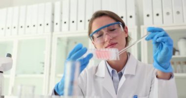 Kadın bilim adamı elinde sıvı olan konteynıra bakıyor. Kimyasal ve farmasötik araştırma ve geliştirme