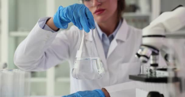 科学家拿着装有透明液体的瓶子 手握着它旋转 用化学透明洁净有毒液体溶剂与科学家手拿着瓶 — 图库视频影像