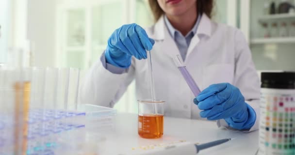 化学科学者は 化学実験室で手の中にオレンジ色の液体でフラスコを保持し 攪拌する 紫色の液体が付いているテスト管を握る実験室の助手 — ストック動画