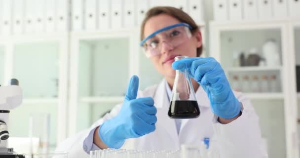 化学工業研究所の科学者は フラスコと親指で黒い液体原油を保持しています 石油製品の品質と承認された検査 — ストック動画
