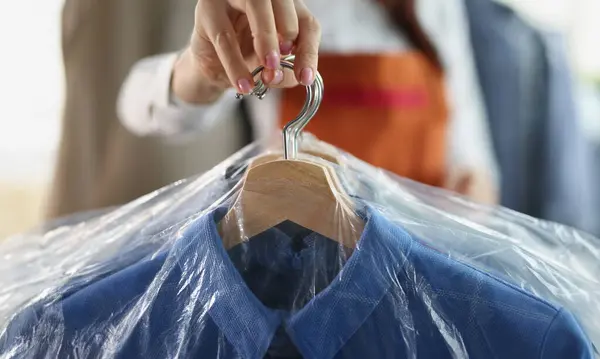 Close-up of worker giving to client clean clothes hanging on hangers at dry cleaning company. Garment packed in plastic bags. Dry cleaning service concept